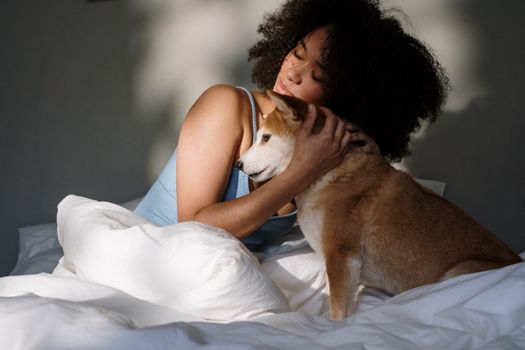 晨光柔和，一位卷发女子抱着她的柴犬坐在床上