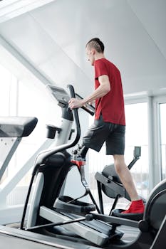 Man using an elliptical trainer in a gym wearing a prosthetic leg. Indoor fitness and health focus.