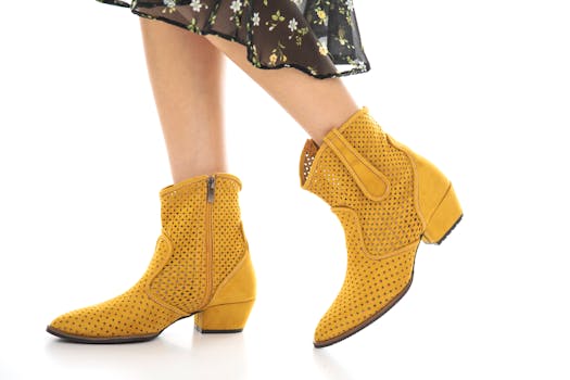 Fashionable yellow ankle boots paired with a floral dress on a clean white background, showcasing trendy footwear design.