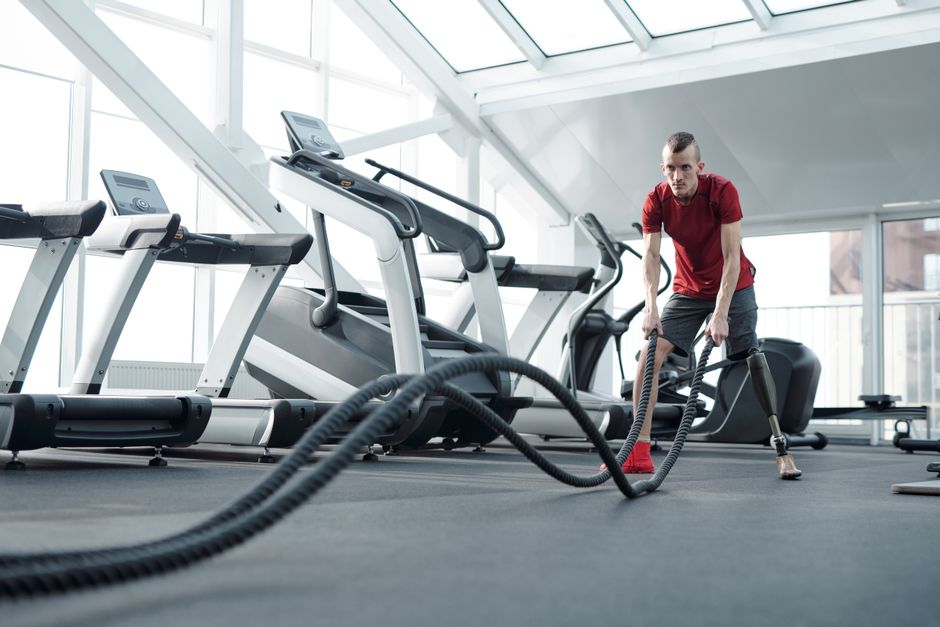 Young man with prosthetic leg working out in a modern gym with battle ropes, showcasing strength and determination.