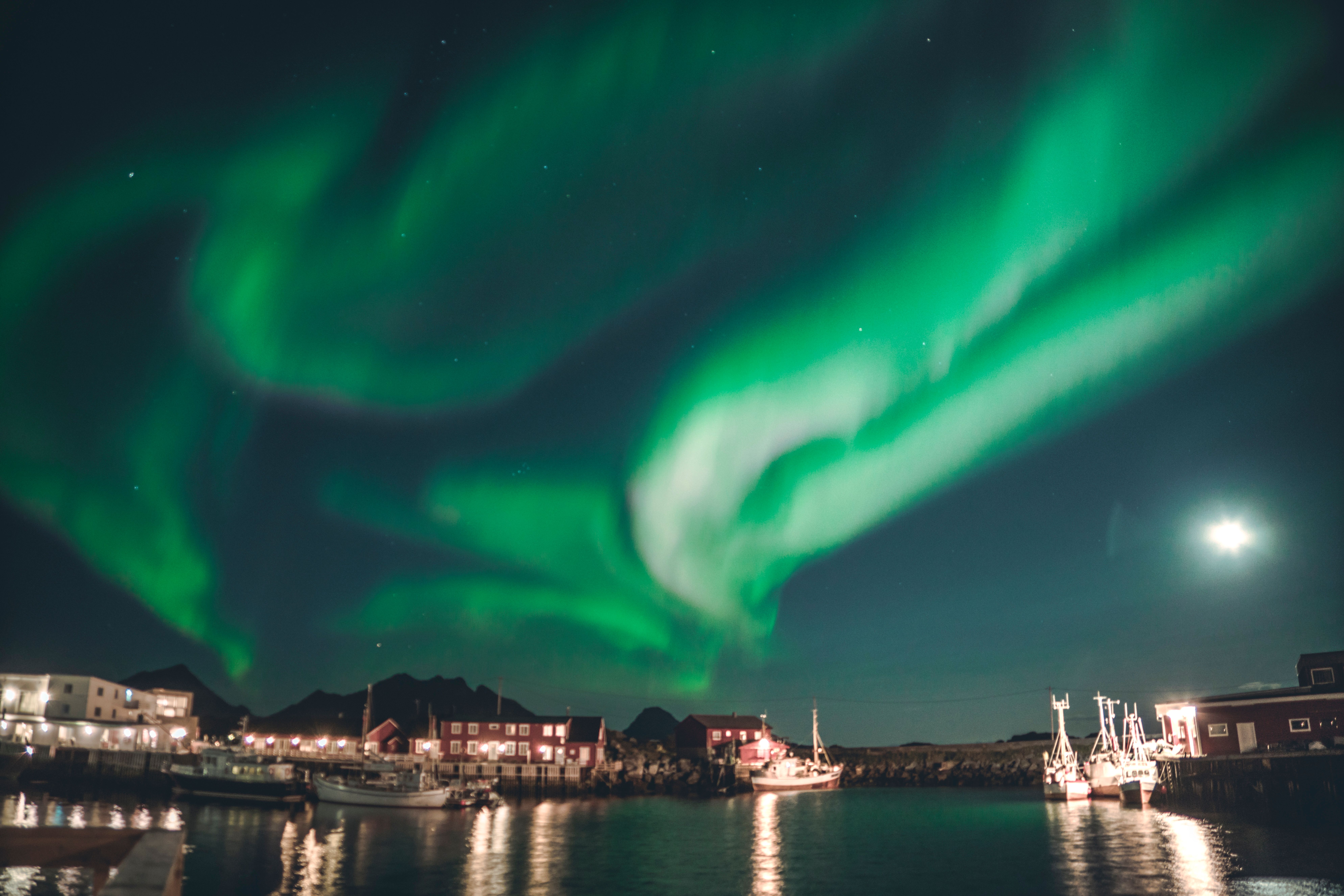 Stunning view of Northern Lights illuminating a tranquil harbor with fishing boats under a clear night sky.