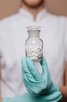 A healthcare worker in gloves holding a clear bottle with pills, symbolizing medical care.