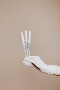 Gloved hand holding sterile syringes for medical use.