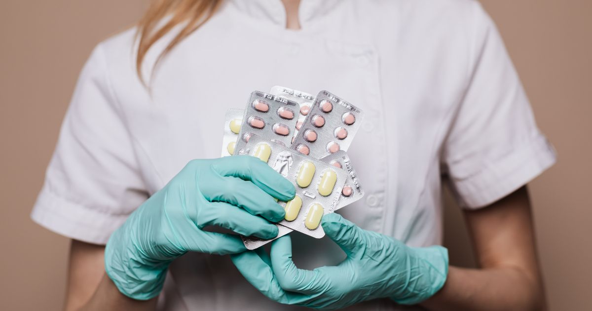 A healthcare professional in gloves holding blister packs of prescription medication