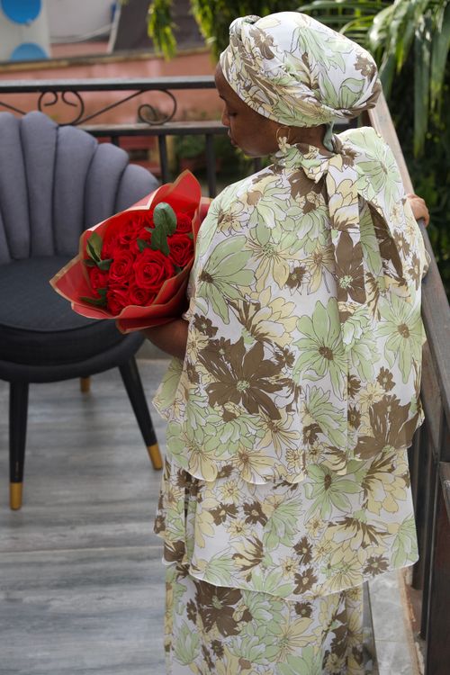 Free African woman in elegant floral attire holding red roses on a balcony in Abuja. Stock Photo