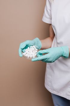 医疗专业人士戴着青色手套，将白色药丸放入培养皿，以强调医疗保健和无菌条件的重要性