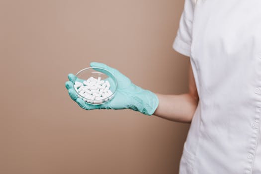 A medical professional in gloves holding a petri dish containing white tablets, highlighting healthcare and medicine.