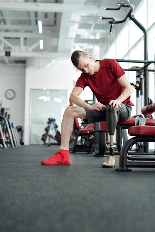 Man in Red T-shirt and Gray Shorts Sitting on Black and Red Exercise Equipment