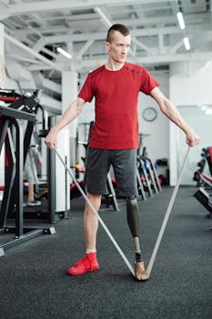 An adult male with a prosthetic leg exercises using resistance bands in a gym setting.