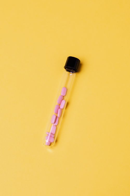 Free A test tube containing pink pills against a vibrant yellow background, depicting healthcare concepts. Stock Photo