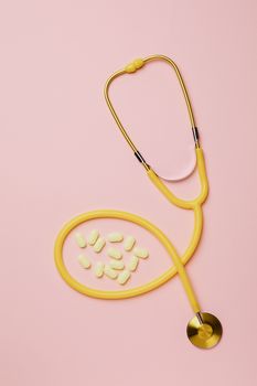 黄色听诊器和药丸置于粉红色背景上，象征着医疗保健和医学