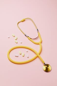 A yellow stethoscope and assorted pills on a pink background symbolize healthcare and treatment.