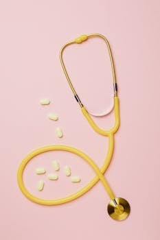 A yellow stethoscope with pills on a pink flat lay setting, symbolizing medical care.