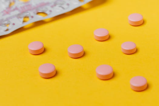 Close-up of pink pills on a vibrant yellow surface, depicting medication themes.