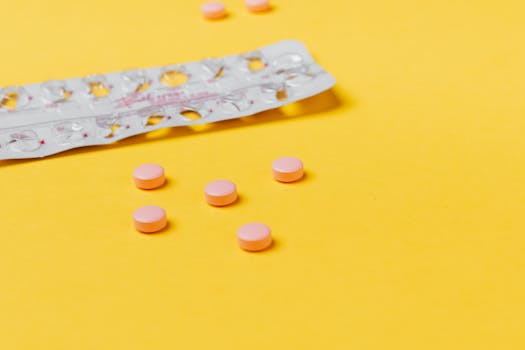 Pink pills scattered on a vibrant yellow background with an empty blister pack.