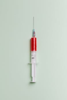 High-quality close-up of a syringe filled with red liquid on a light background.