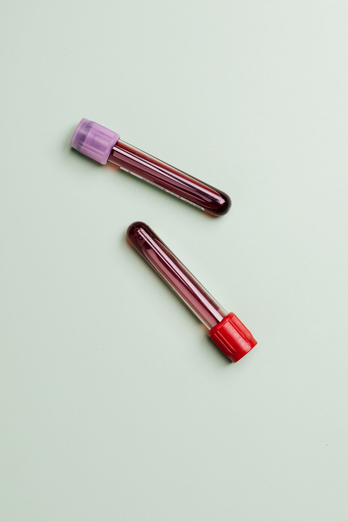 Two capped blood sample tubes on a pale green background