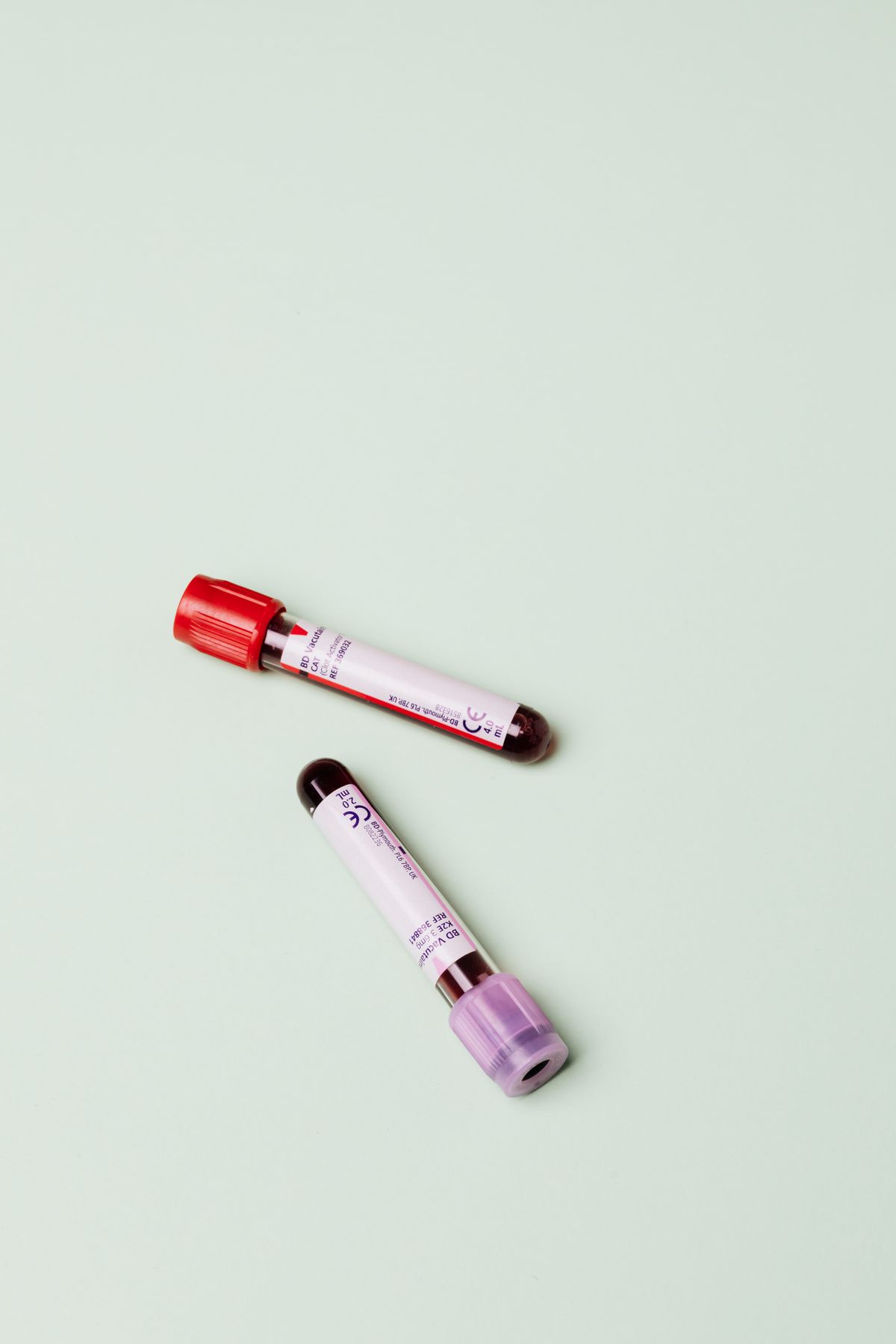 Two capped blood sample tubes lying on a pale green background