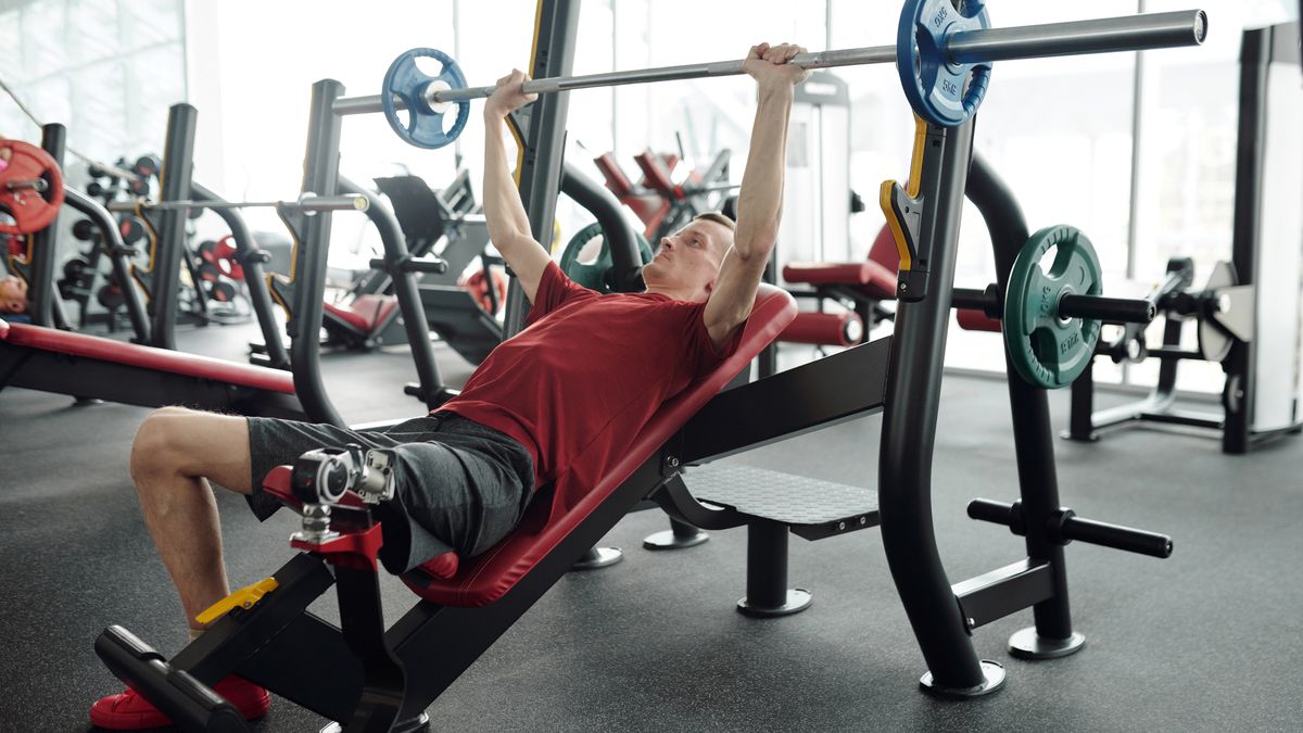 A man with a prosthetic leg lifting weights on an incline bench in a gym setting.