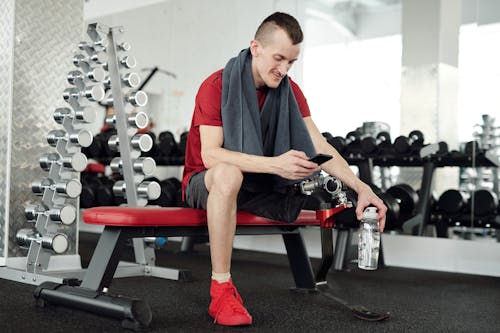 Man in Red and Black Polo Shirt and Black Pants Sitting on Red and Black Exercise Bench