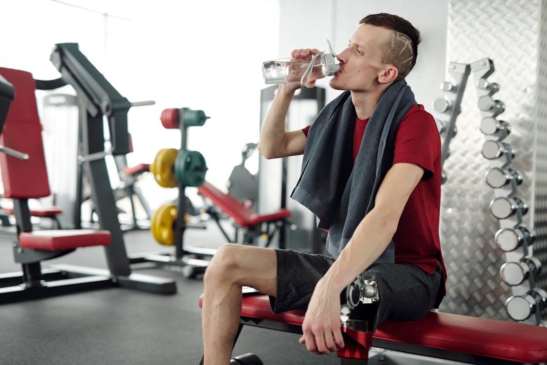 Free Man in Black and Red Crew Neck T-shirt Sitting on Black and Red Exercise Equipment Stock Photo
