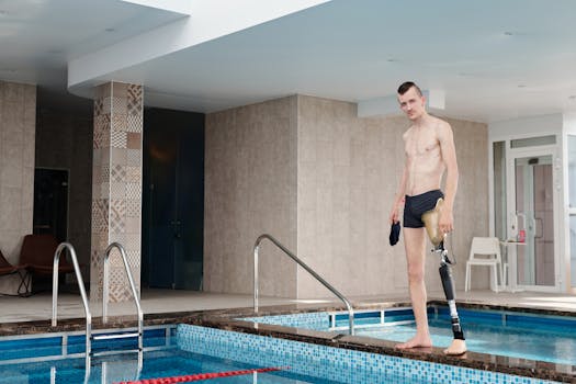 A confident young man with a prosthetic leg stands by an indoor swimming pool, ready for a swim.