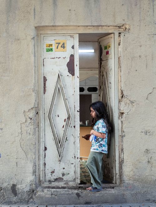 Free Girl standing at a weathered doorway in Tehran, Iran, showcasing urban life. Stock Photo