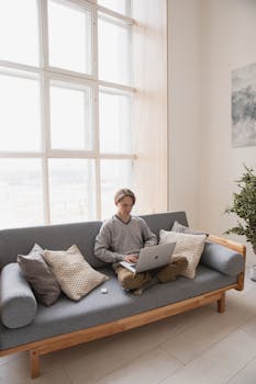 Man working remotely on a laptop while lounging on a couch in a cozy home setting.