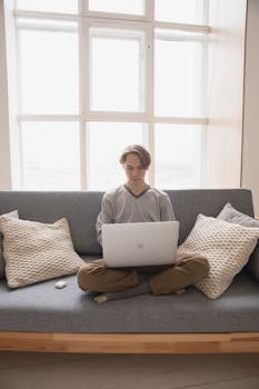 Man sitting cross-legged on a couch using a laptop, epitomizing remote work lifestyle at home.