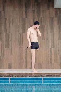 A determined male amputee swimmer stands at the poolside, ready for a swim.