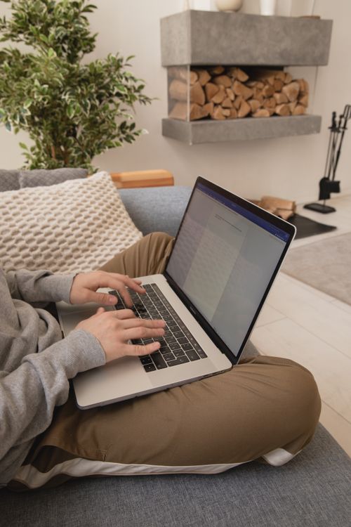 Free Person working on a laptop in a comfortable home setting with a modern fireplace. Stock Photo