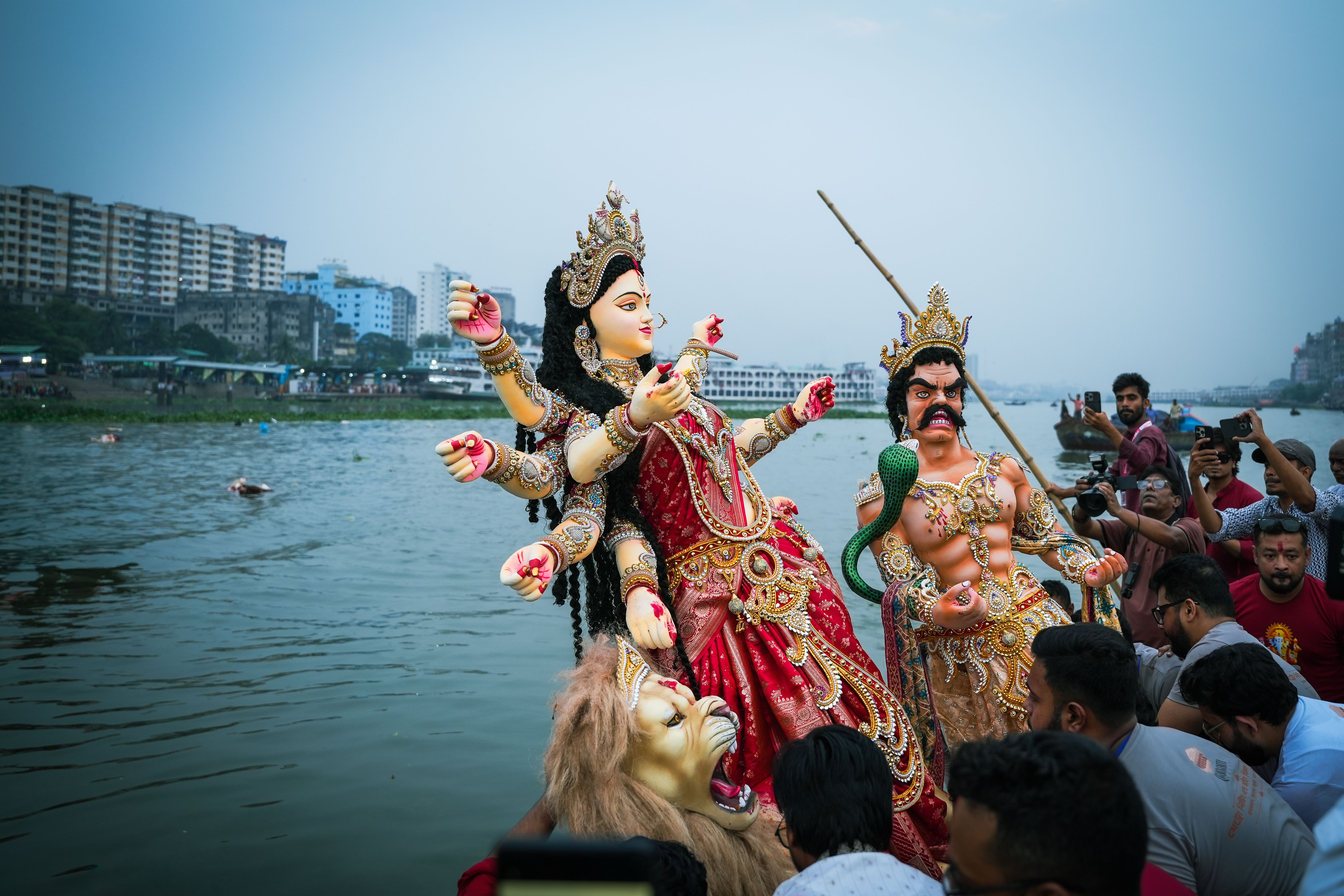 People celebrate Durga Puja with vibrant statues by the river in Dhaka, Bangladesh.