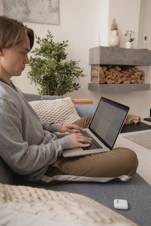 Free A young man typing on a laptop while sitting on a comfortable couch in a cozy living room. Stock Photo