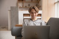 一位年轻人在家中的沙发上微笑着使用笔记本电脑，象征着远程工作和数字生活方式