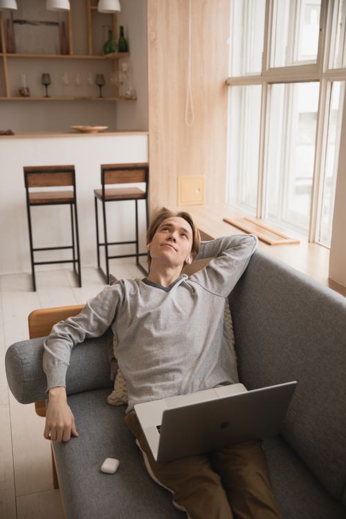 Free A young man relaxes with a laptop on the sofa in a modern living room. Stock Photo