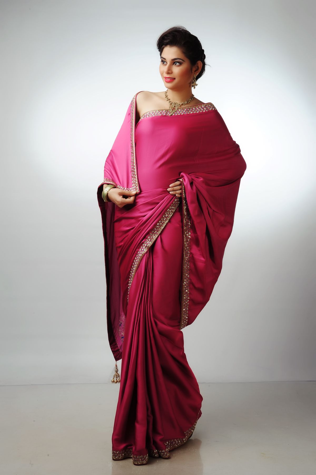 Woman in a rani-pink saree with a gold border, posing in a bright studio