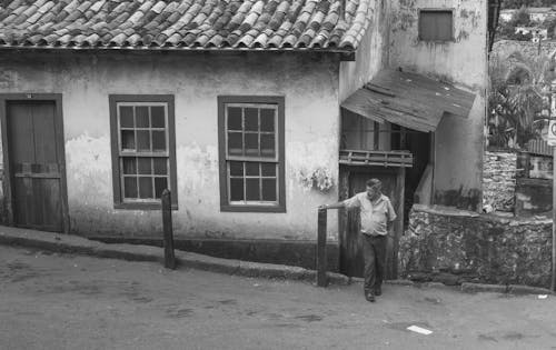 Monochrome Photograph of a Man Standing in Front of a House
