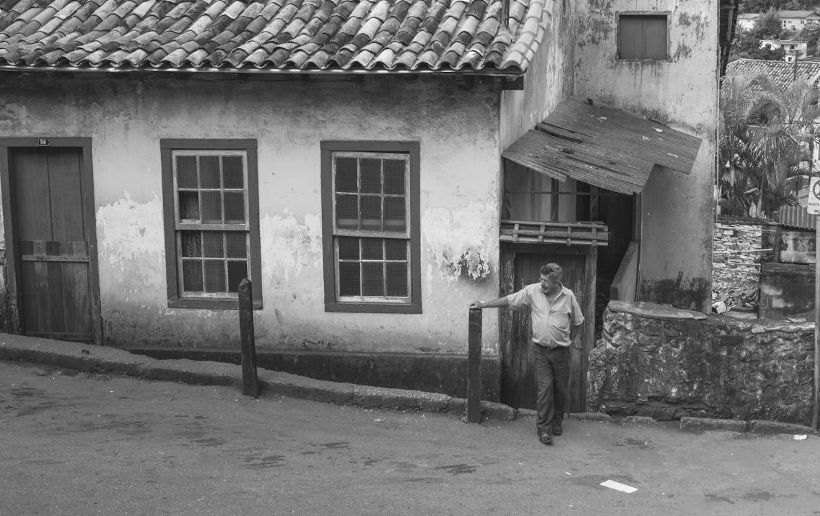 Monochrome Photograph of a Man Standing in Front of a House