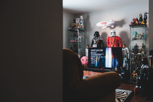 Interior of hipster style room with computer screen near glass shelves with assorted toy robots and hanging plane in front of cozy armchair with carpet on floor