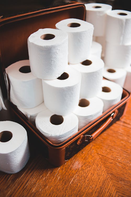 From above of heap of similar white toilet paper rolls with soft texture in leather suitcase on wooden floor in apartment during COVID 19 pandemic