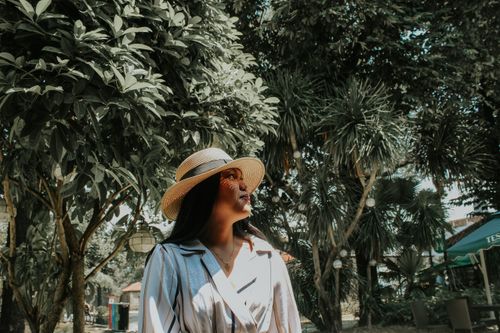Free Elegant woman in a straw hat posing under trees in a garden setting. Stock Photo