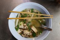 Authentic Asian noodle soup garnished with pork slices and green herbs, served with chopsticks.