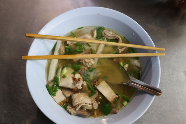 Noodle soup with herbs and chopsticks resting across a white bowl — photo by M Snedelrev on Pexels