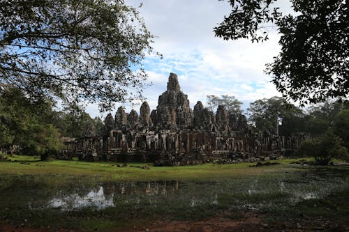 Free Scenery view of aged church complex exterior on green field near rippled pond and growing trees under cloudy sky in Cambodia Stock Photo