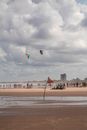 Wet sandy sea shore with flag on wooden stick and flying kites under cloudy sky with group of anonymous travelers on bikes during summer vacation