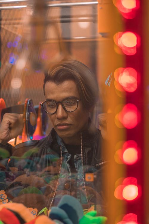 Free A man looks wistfully through glass, surrounded by vibrant bokeh lights. Stock Photo