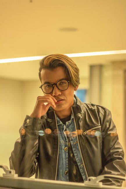 Portrait of a man wearing eyeglasses and a leather jacket indoors, reflecting an introspective mood.