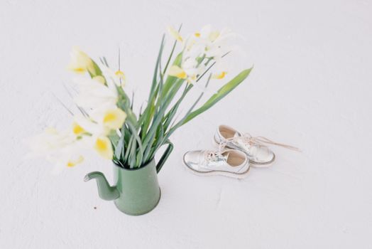 Flower bouquet in pitcher near glossy sneakers on white background