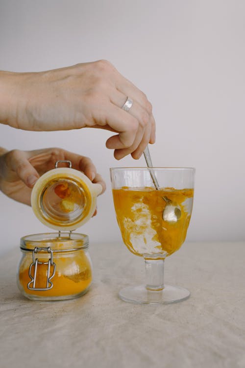 Crop hands adding turmeric in glass of hot water in morning Stock Photo