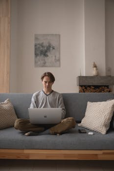 Man sitting on a couch using a laptop in a warm, cozy living room, perfect for remote work.